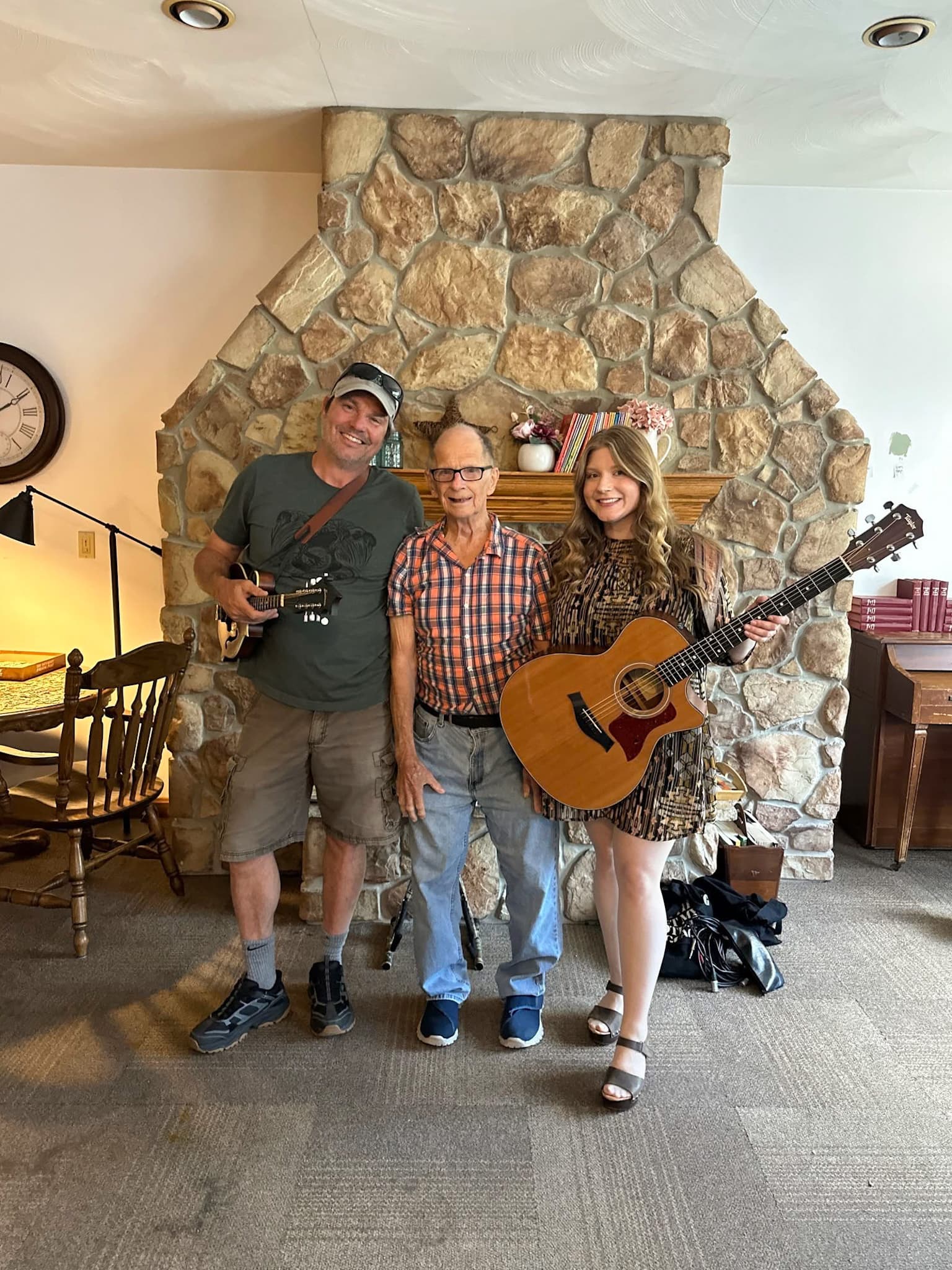 A Pine View resident by the stone fireplace with two visiting musicians holding guitars